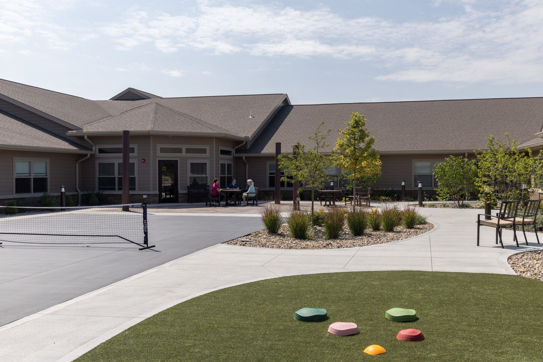 Exterior of a beige building with a walkway, small garden, and artificial turf with colorful stepping stones.