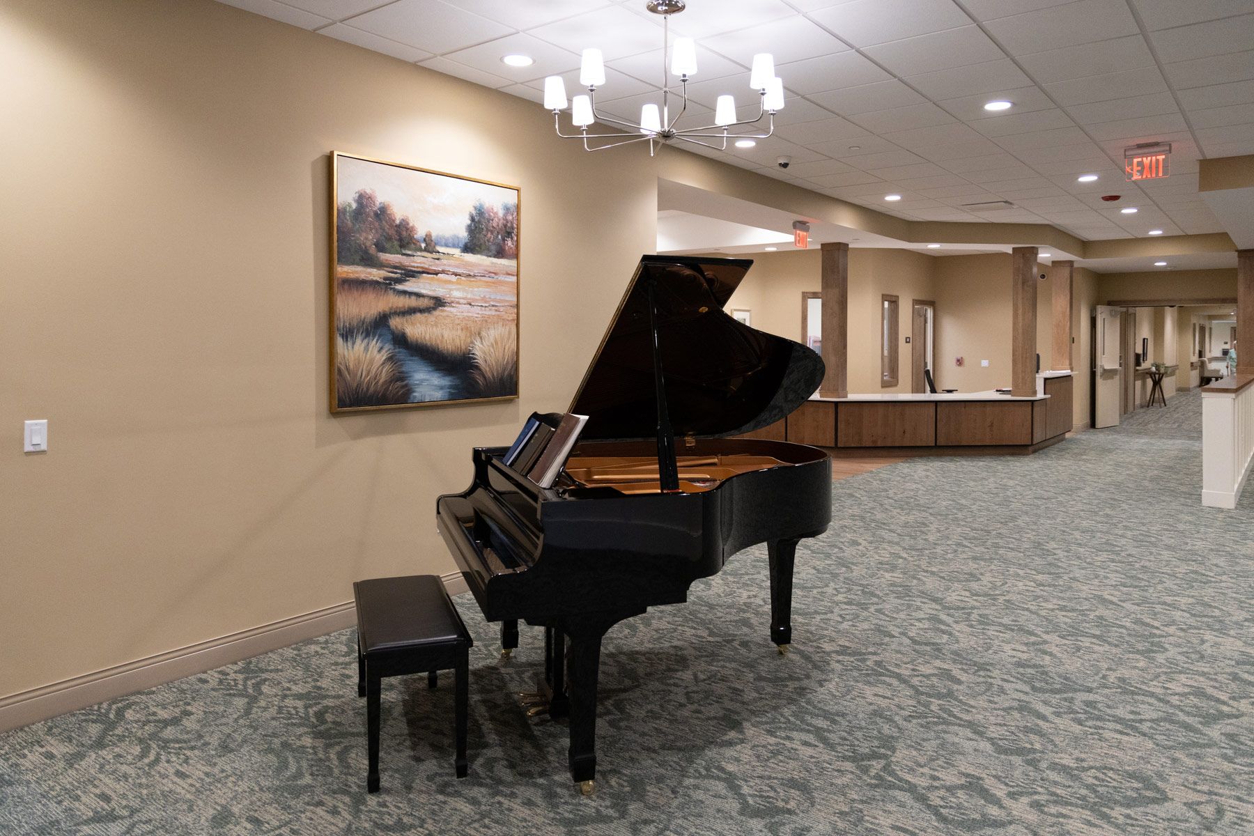 Grand piano in a hallway with a painting, bench, chandelier, and a long hallway with a counter.