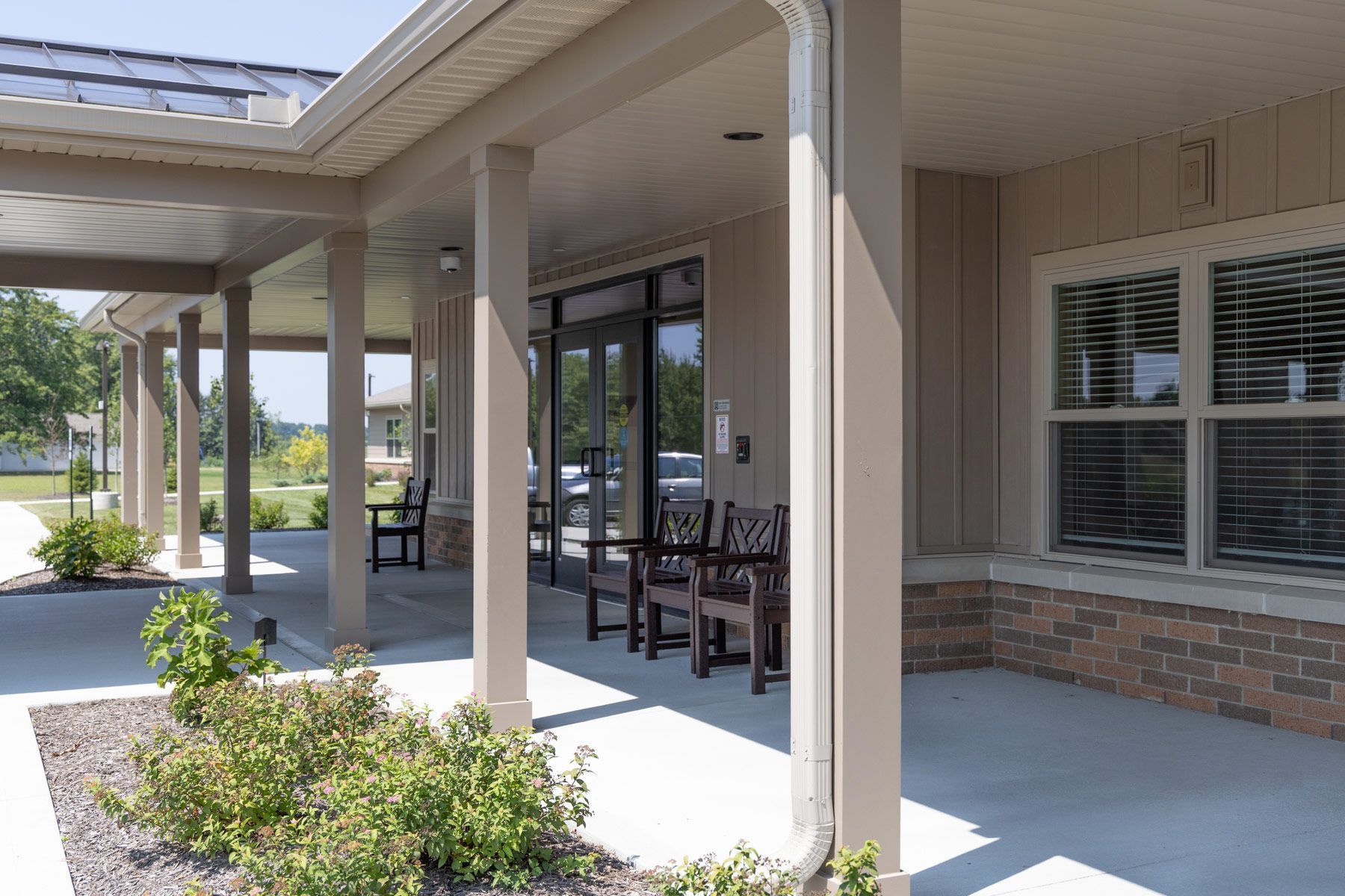 Covered porch with seating, entrance to a building. Light beige columns, brick accents, and windows.