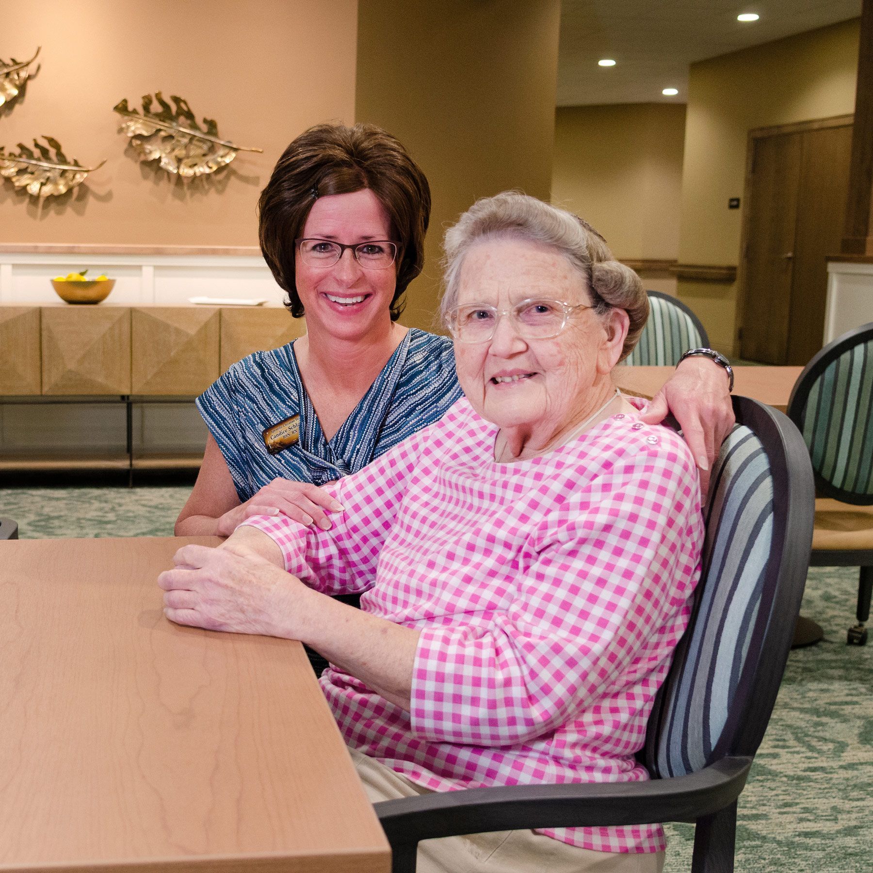 Smiling woman with eyeglasses and caregiver sitting at a table.