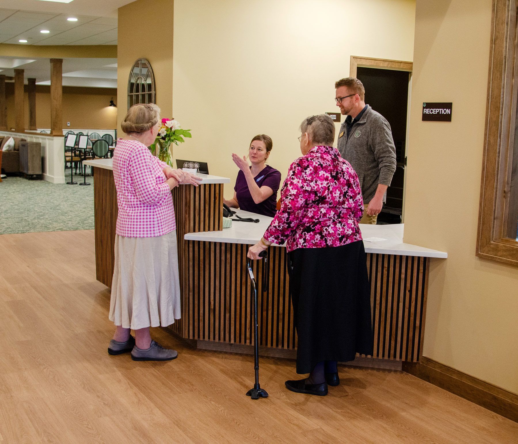 Reception desk with staff assisting two women. One woman uses a cane.