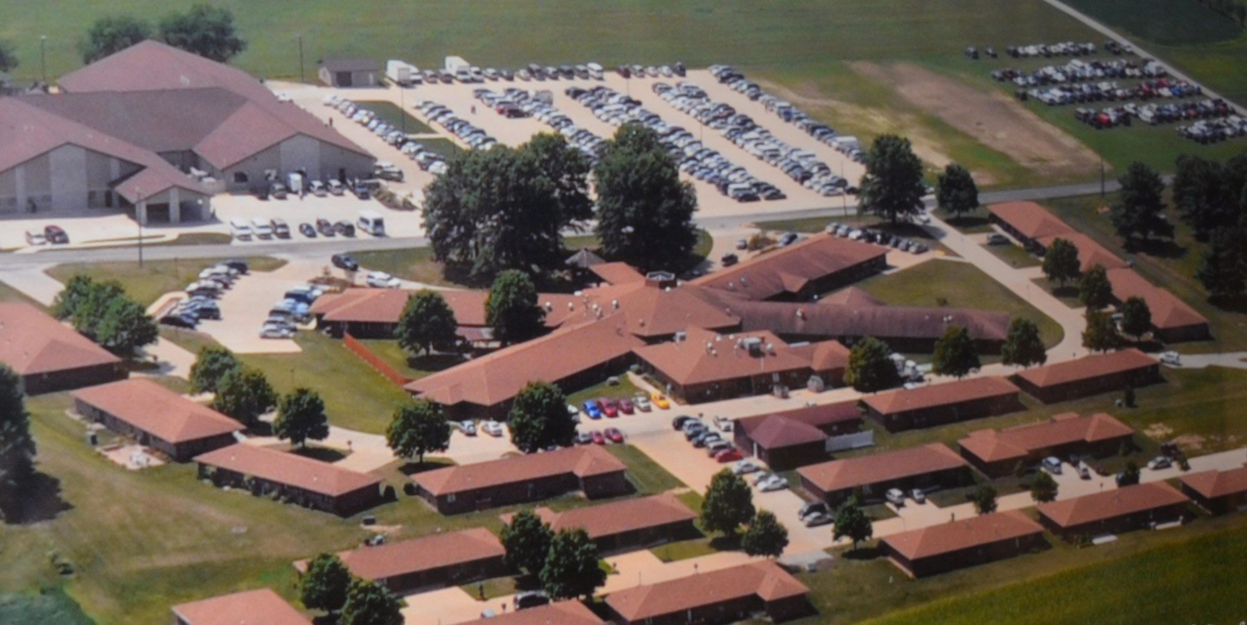 Aerial view of a complex with multiple buildings, parking lots, and a large open field.