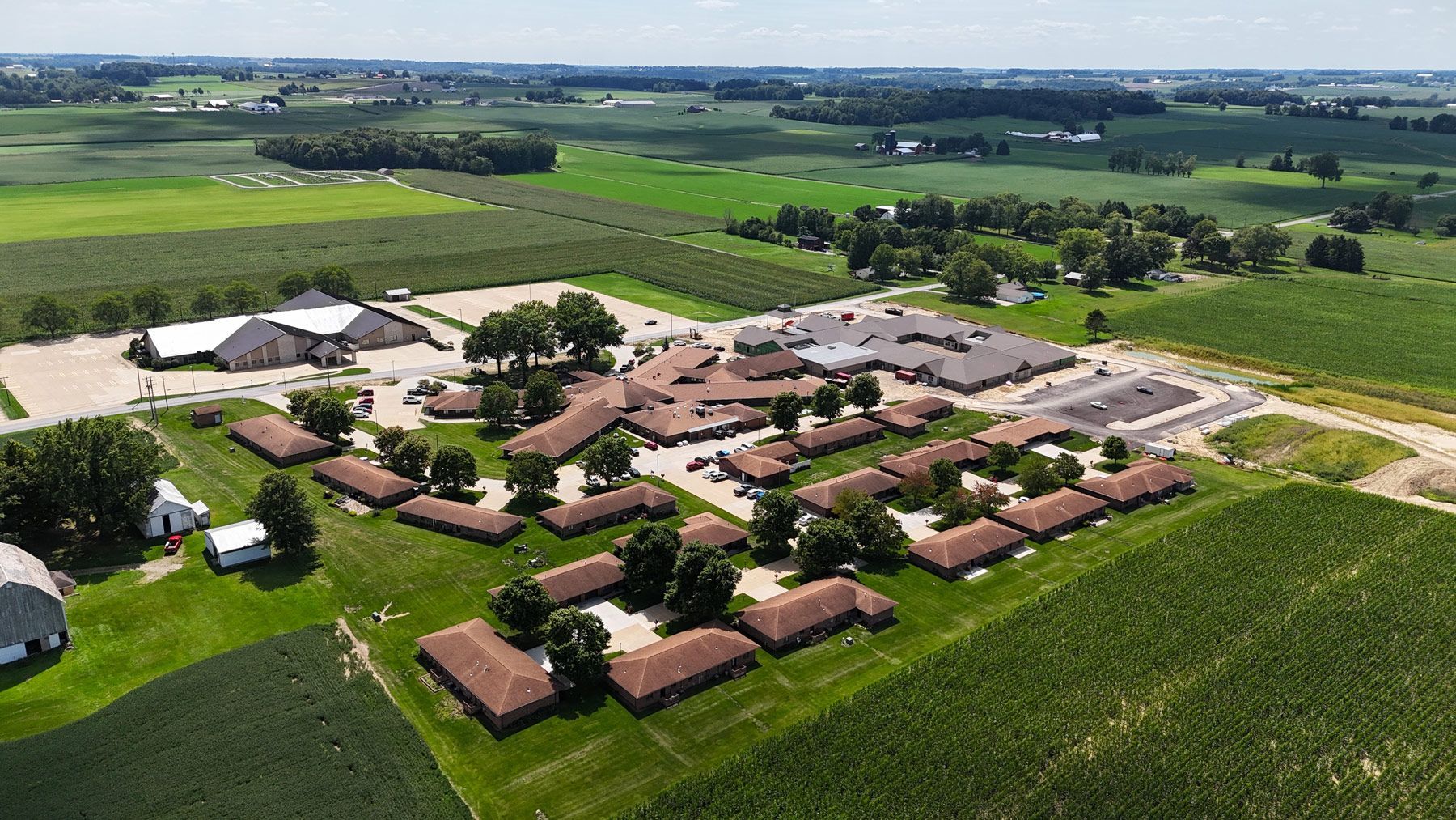 Aerial view of a rural complex with multiple buildings, surrounded by fields and trees.