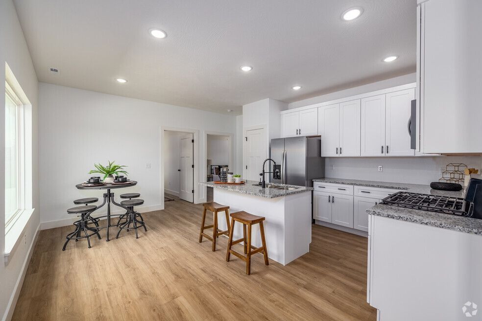 a kitchen with white cabinets , a refrigerator , a stove , a table and stools .