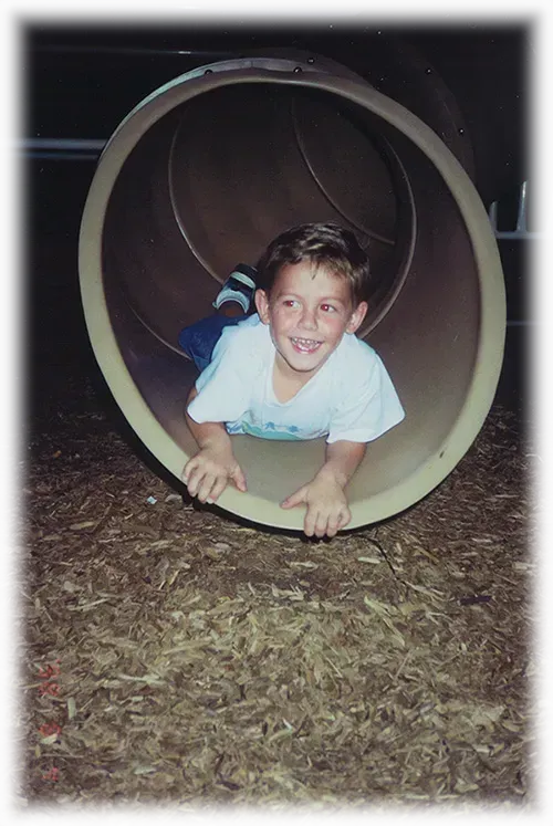 A young boy is crawling through a tube at a playground.