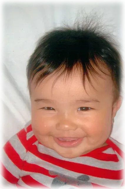 A baby wearing a red and gray striped shirt is smiling.
