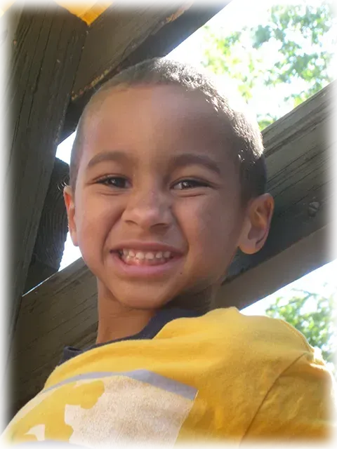 A young boy in a yellow shirt smiles for the camera.