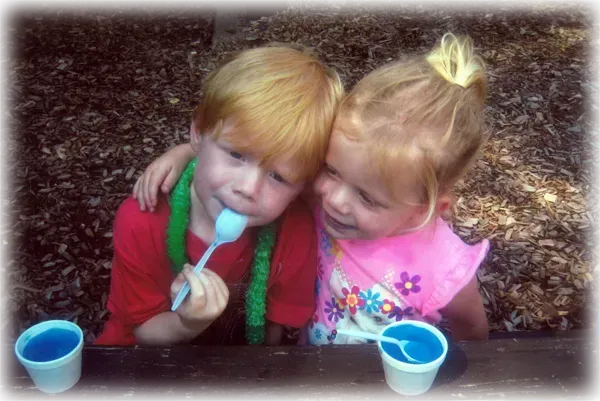 A boy and a girl are eating ice cream with plastic spoons.