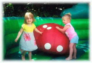 Two little girls are playing with a large red ball in a bouncy house.
