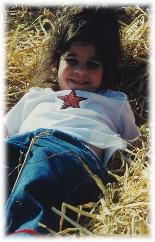 A little girl is laying in a pile of hay.