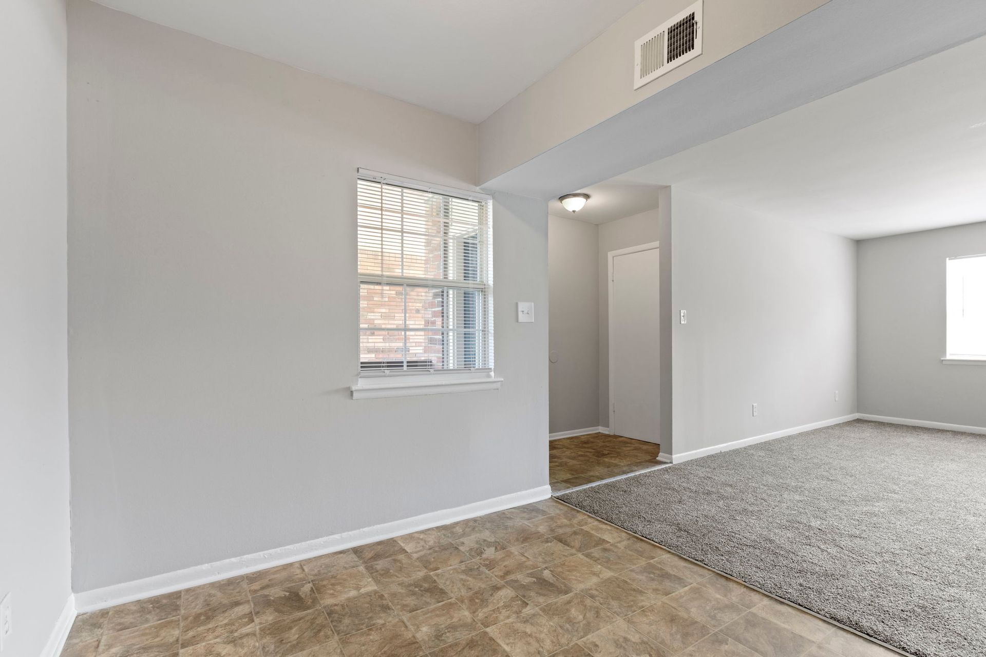 Empty living room with gray walls, a window, and a doorway leading to the hallway with carpet.