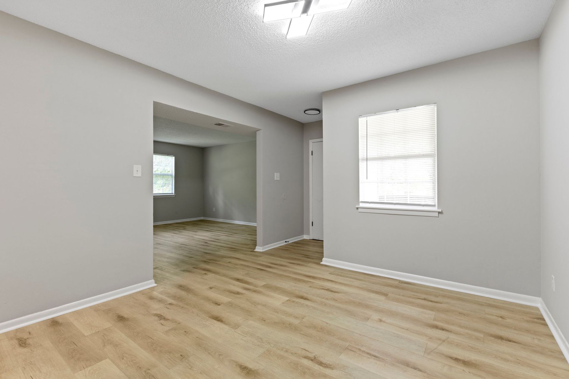 Empty room with light wood floors, gray walls, and a window with blinds.