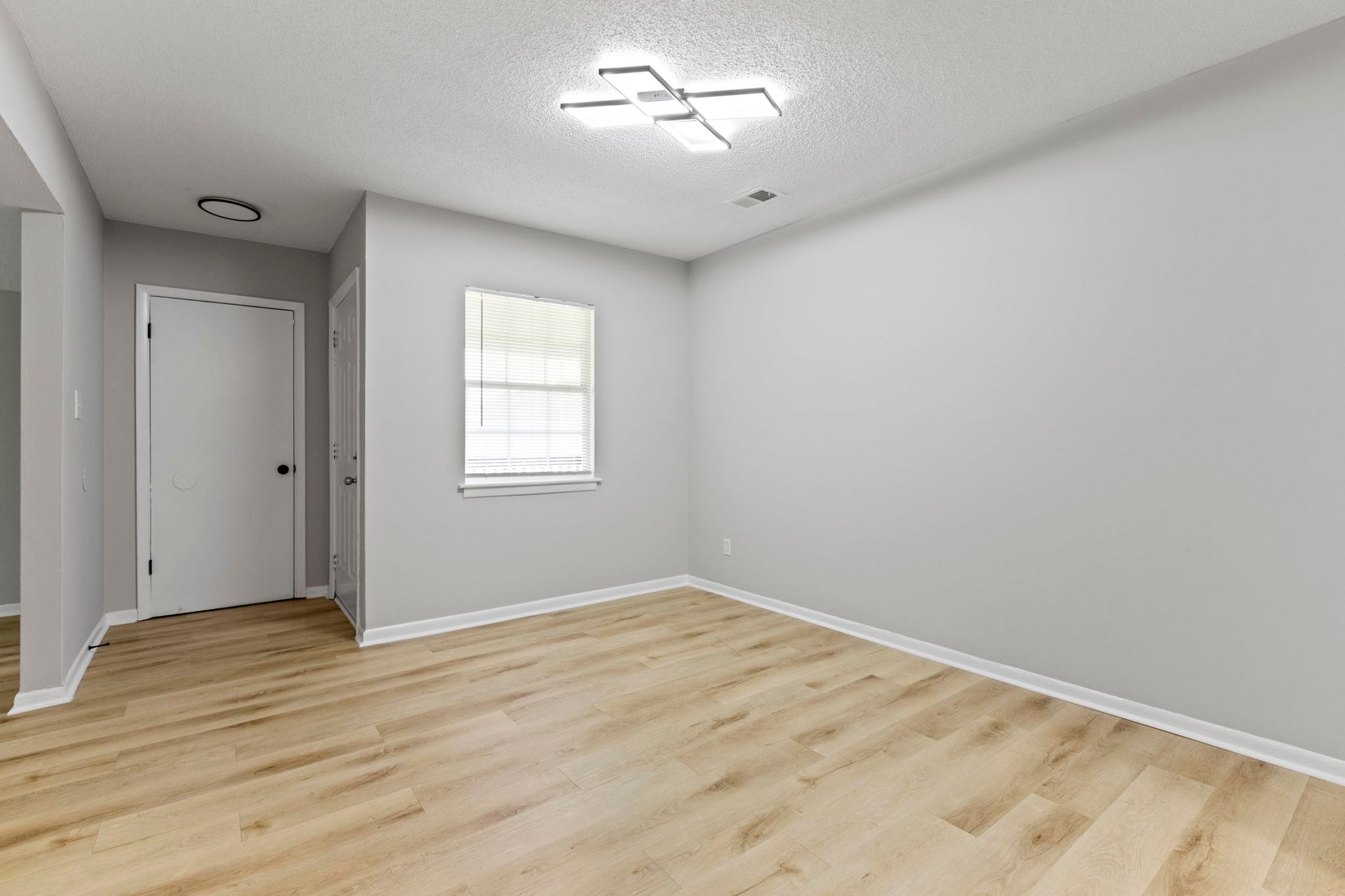 Empty room with light gray walls, wood-look floor, white door, and a small window.