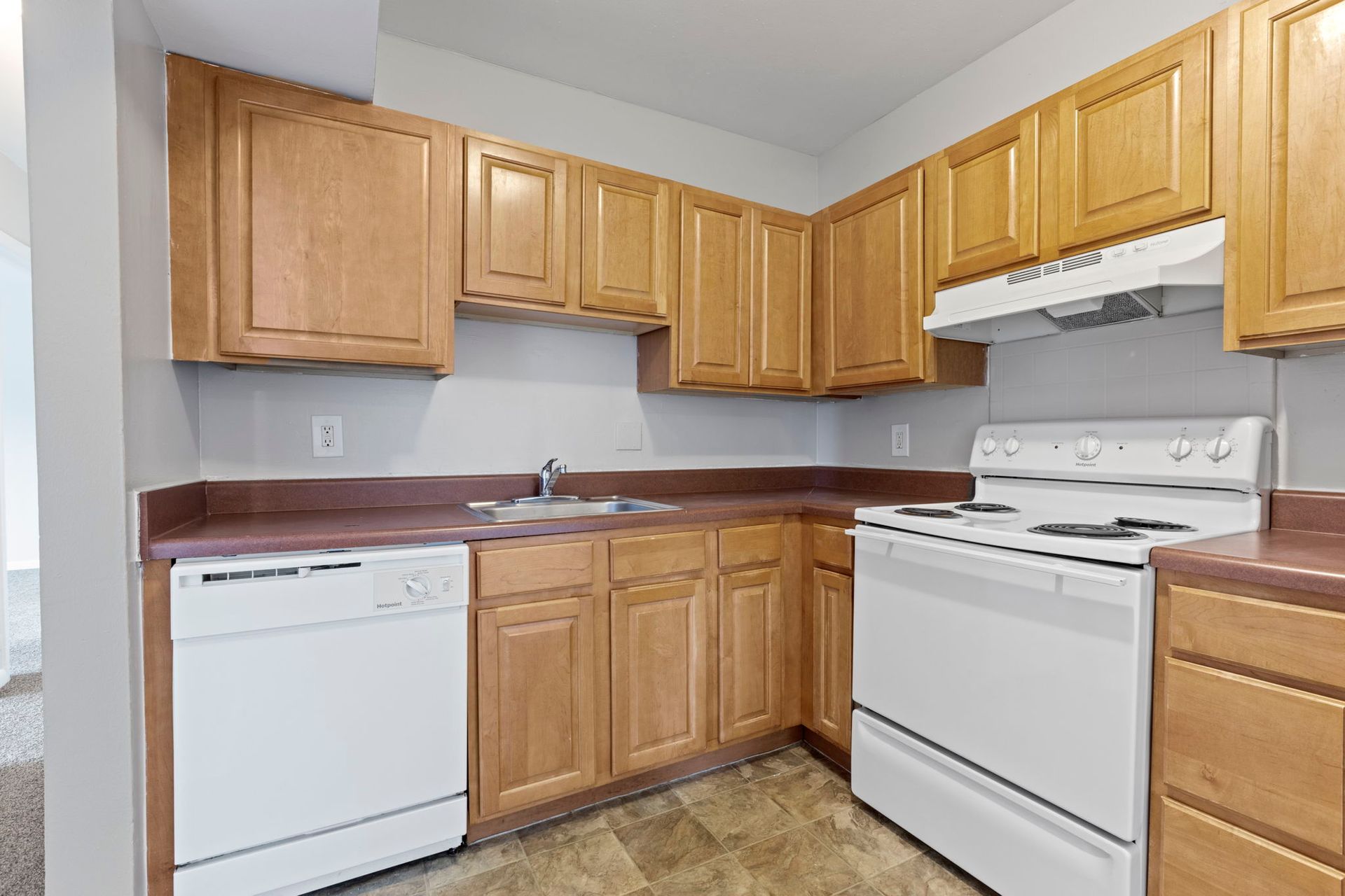 Kitchen with light wood cabinets, white appliances, and maroon countertops.