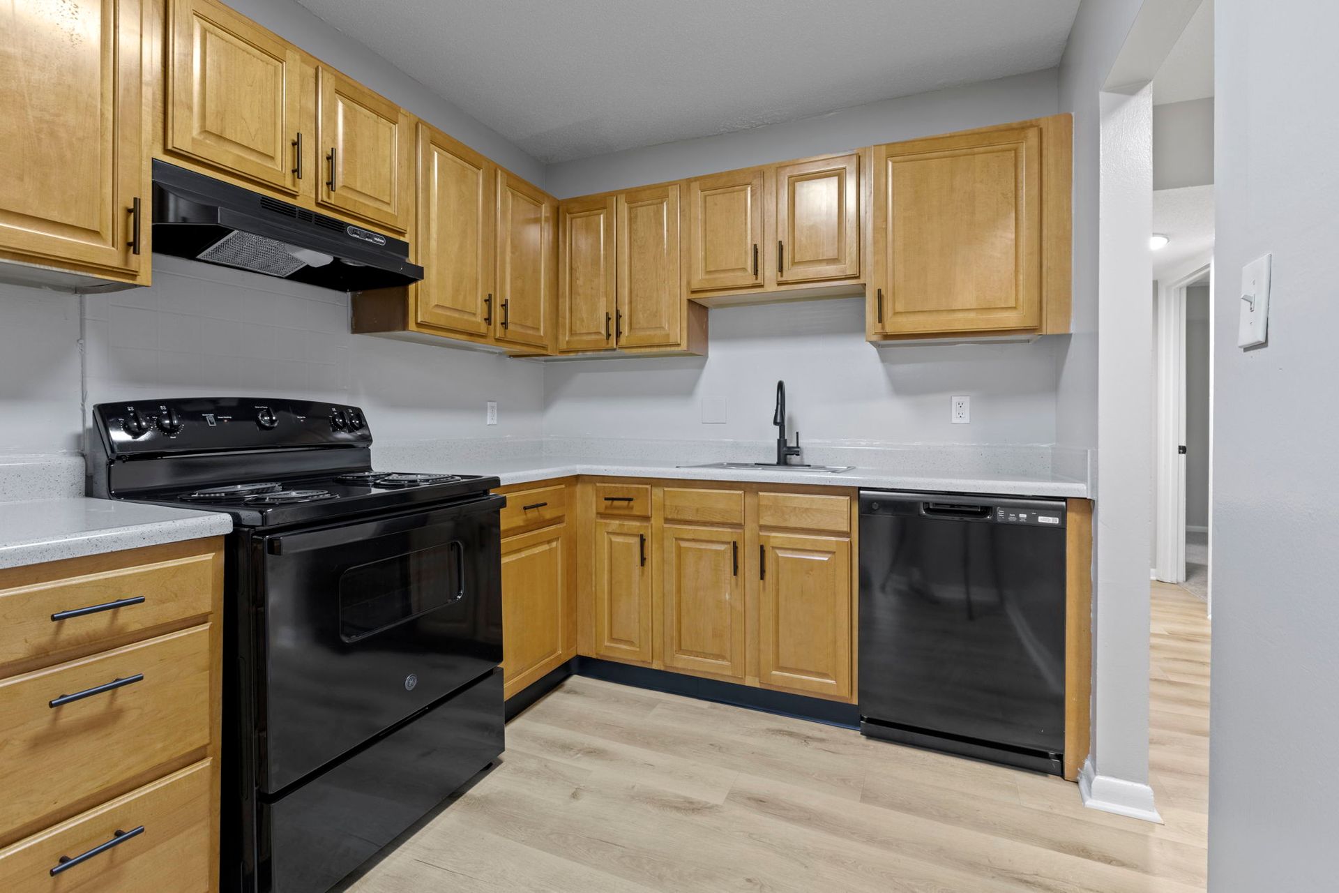 Kitchen with light wood cabinets, black appliances, and light gray walls and countertops.