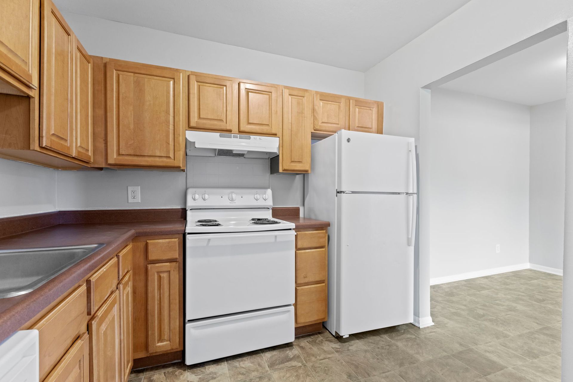 Kitchen with light wood cabinets, white appliances, and a doorway to another room.
