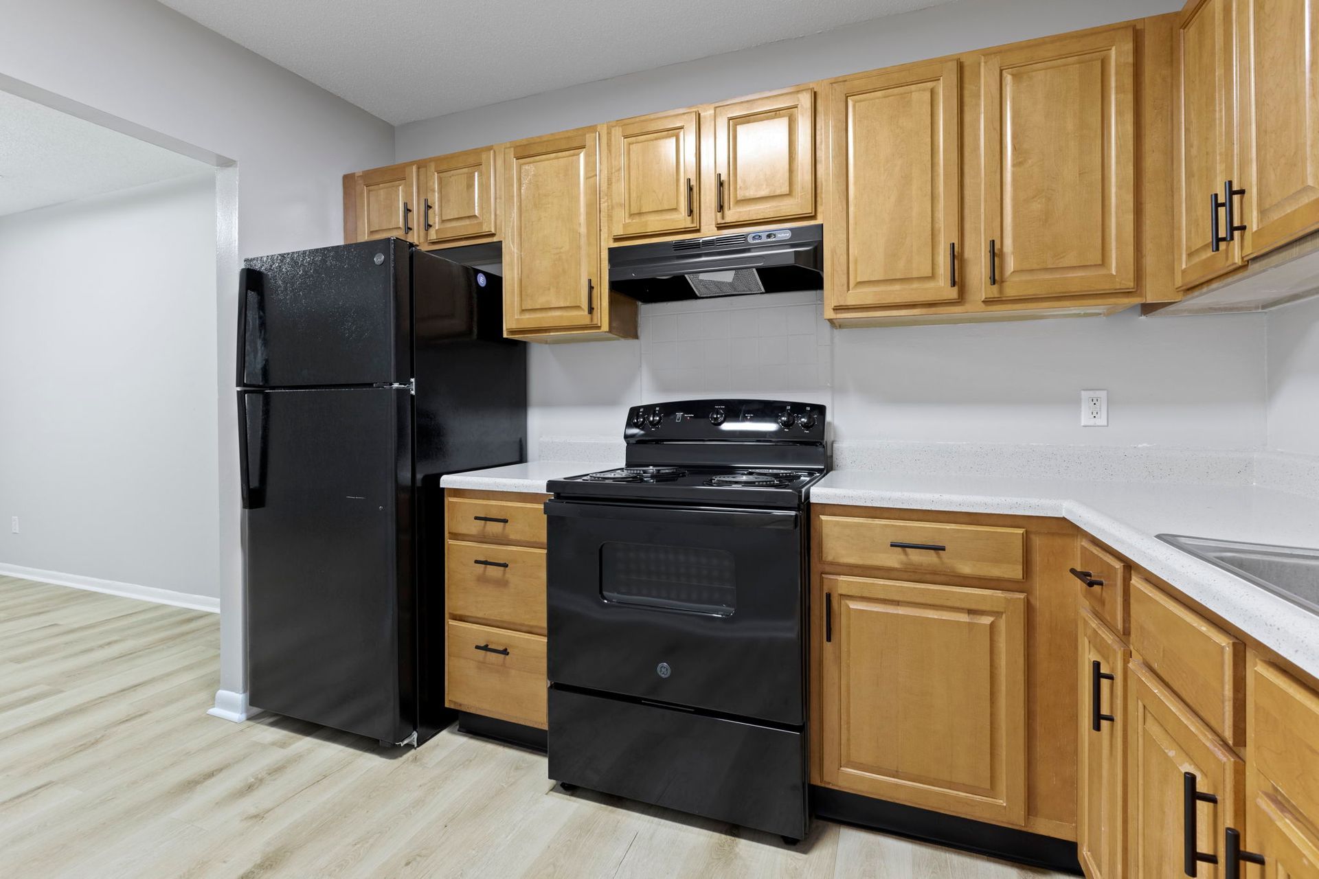 A kitchen with black appliances and wood cabinets; a refrigerator, oven, and cabinets.