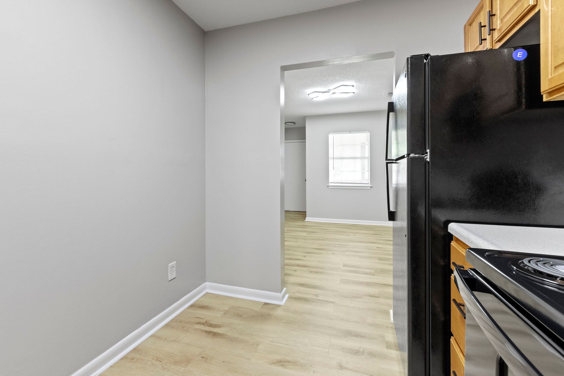 Kitchen with gray walls, black appliances, and doorway leading to another room with window.