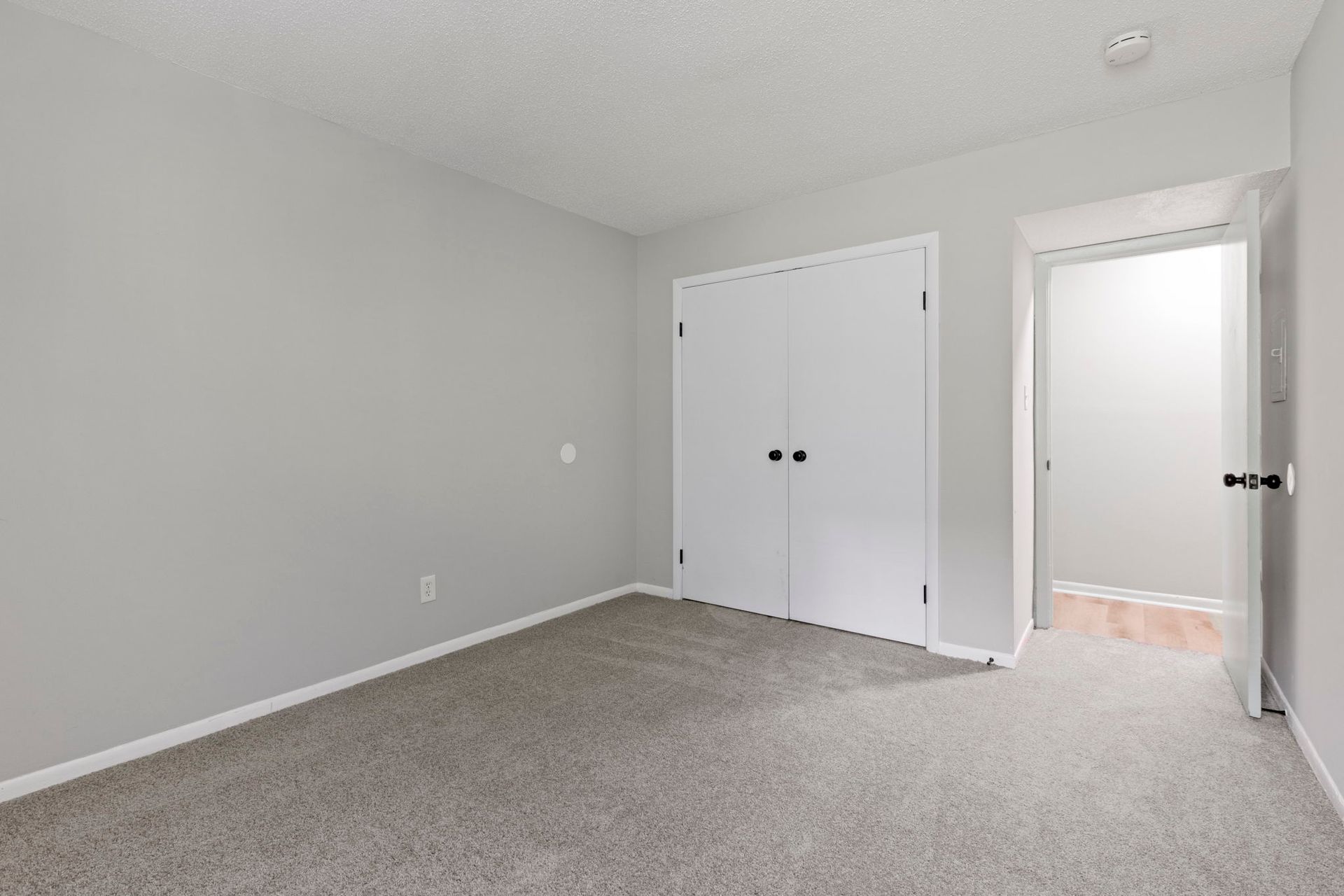 Empty bedroom with gray walls, white closet, and doorway to a hallway. Gray carpet.