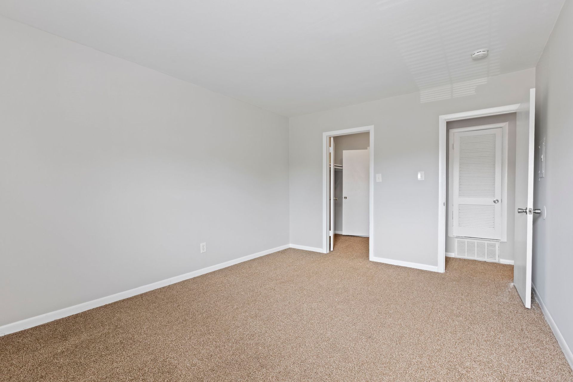Empty bedroom with beige carpet, light gray walls, and two open doorways.