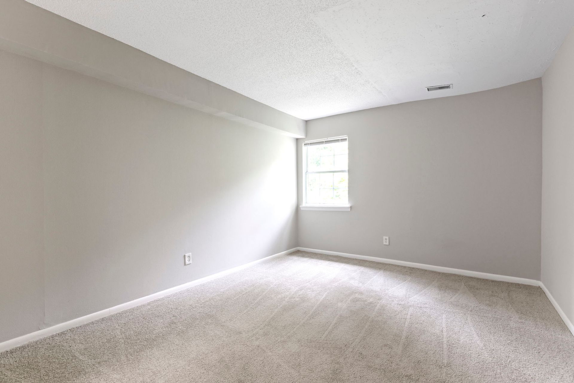 Empty room with gray walls, white ceiling, carpet, and a small window.