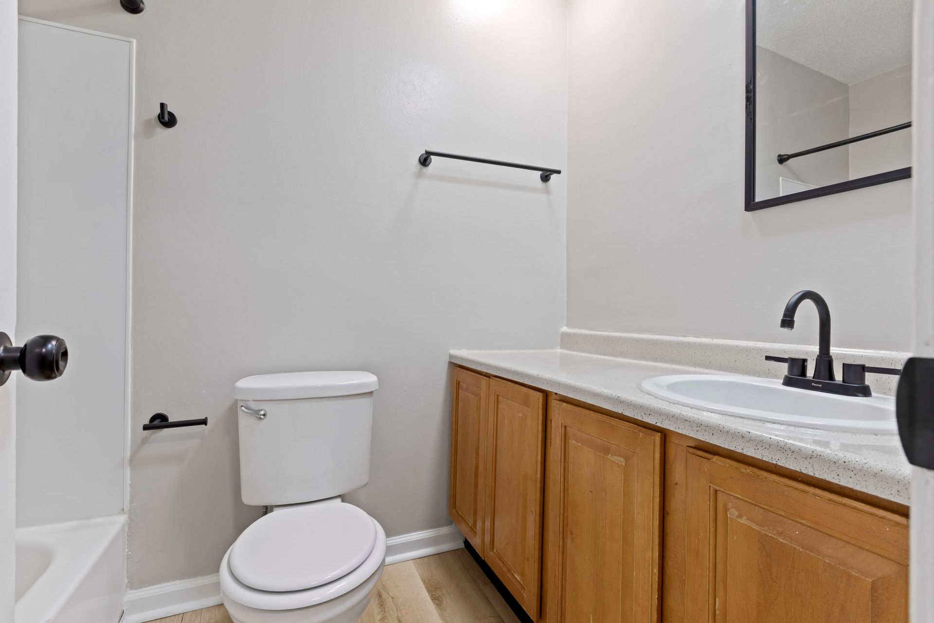 Bathroom with a white toilet, light wood vanity, and black fixtures.