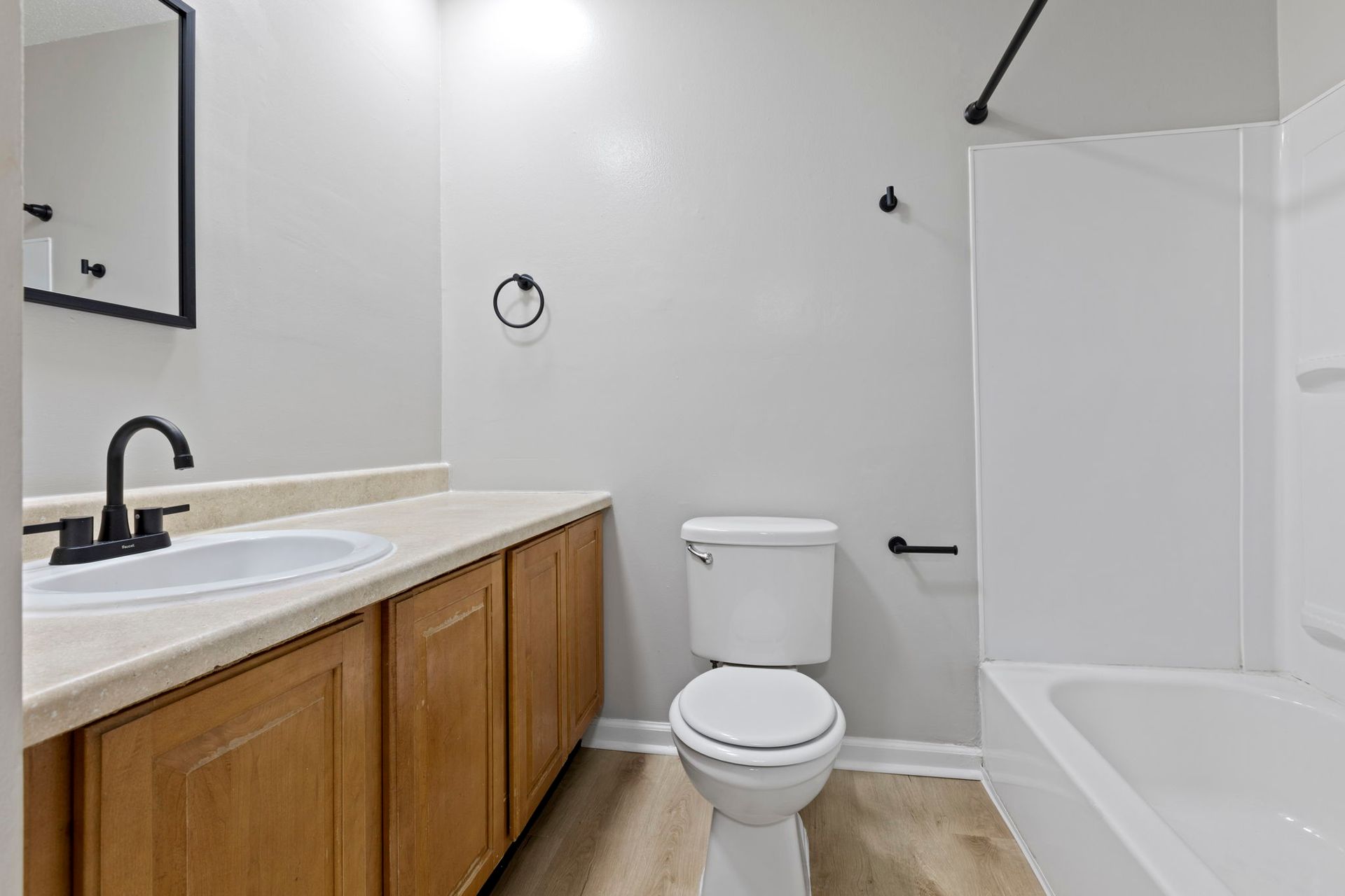 Bathroom with a white toilet, tub, and sink with black fixtures and wood cabinets.
