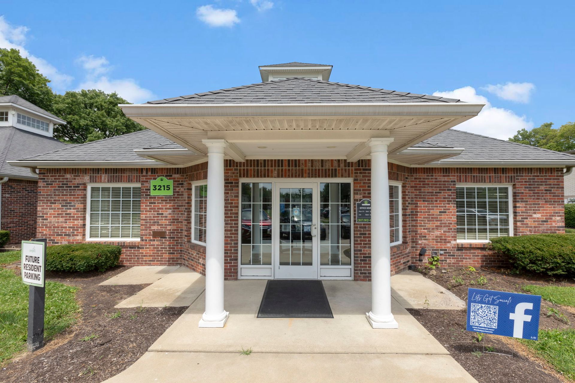 Brick building entrance with white pillars and glass doors. Green sign above door. Blue Facebook sign.