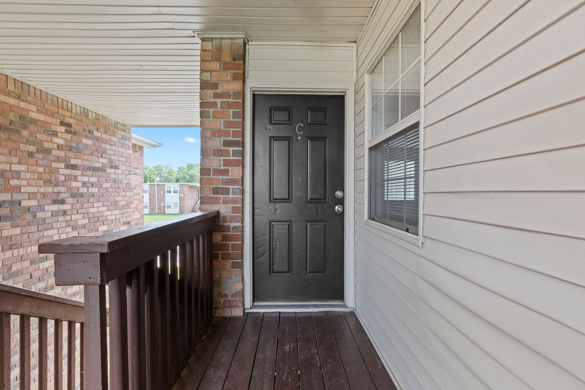 Covered porch with black door, brick pillar, and white siding.