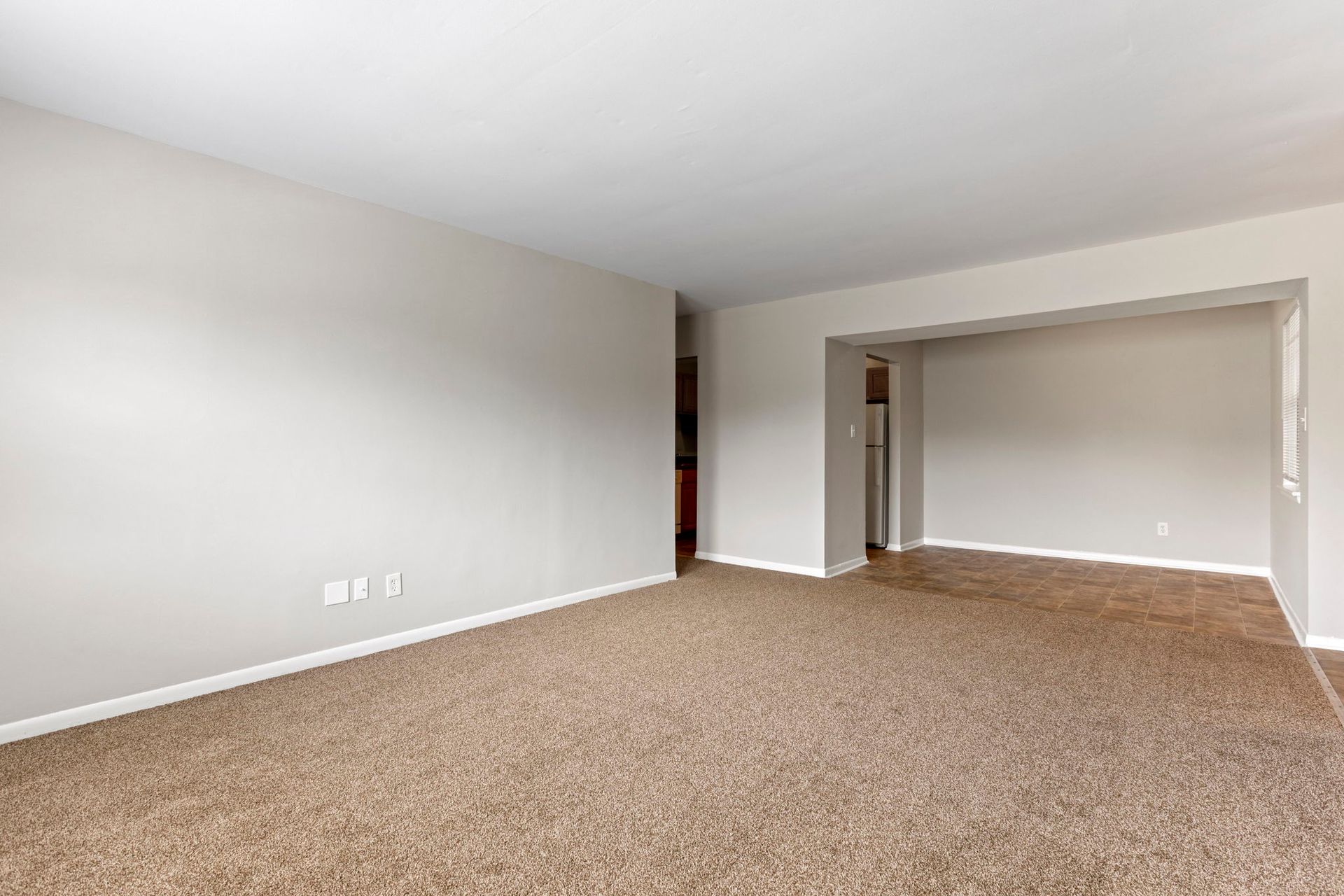 Empty living room with beige carpet and light gray walls; doorway on right.