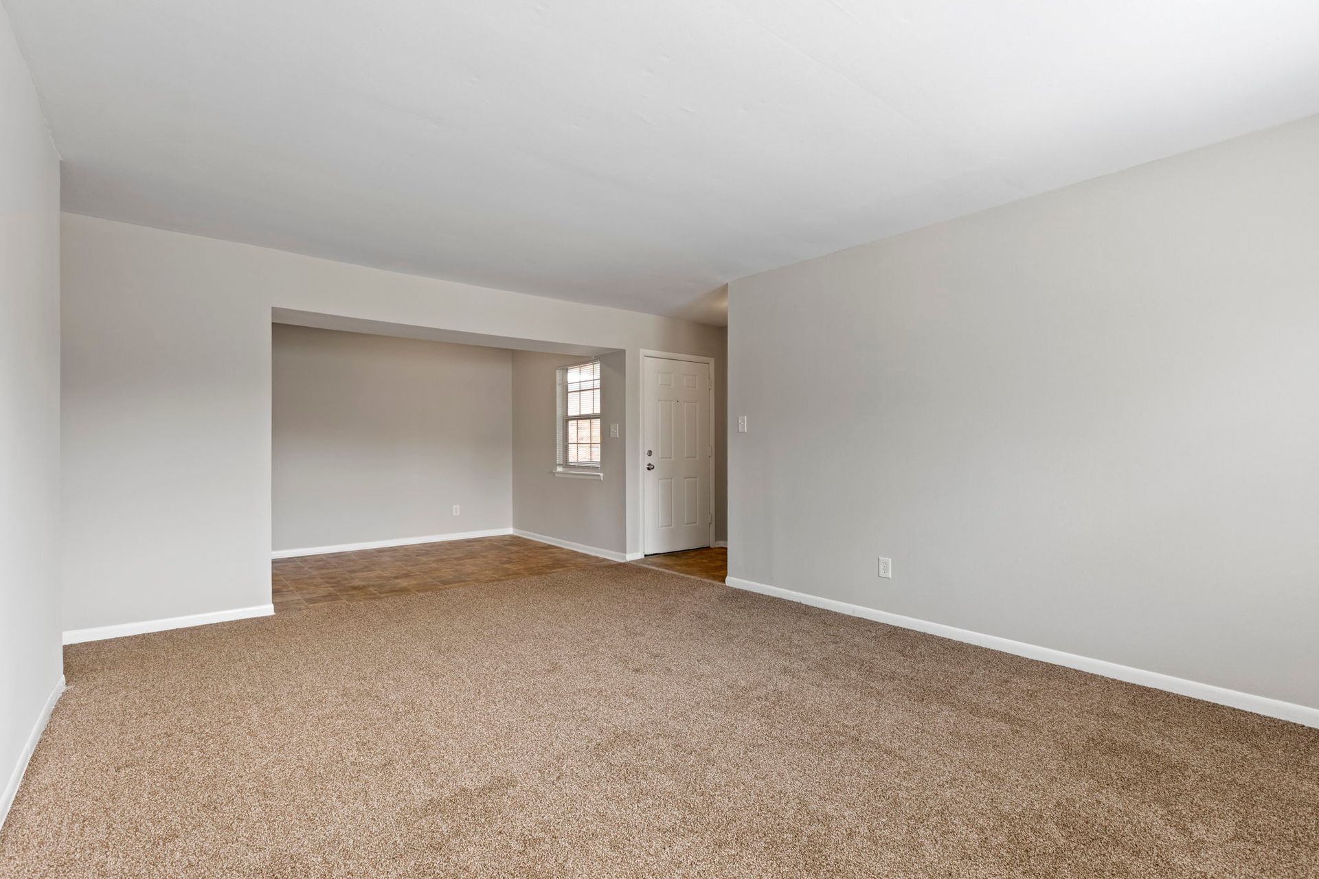 Empty living room with beige carpet, light gray walls, and a doorway.