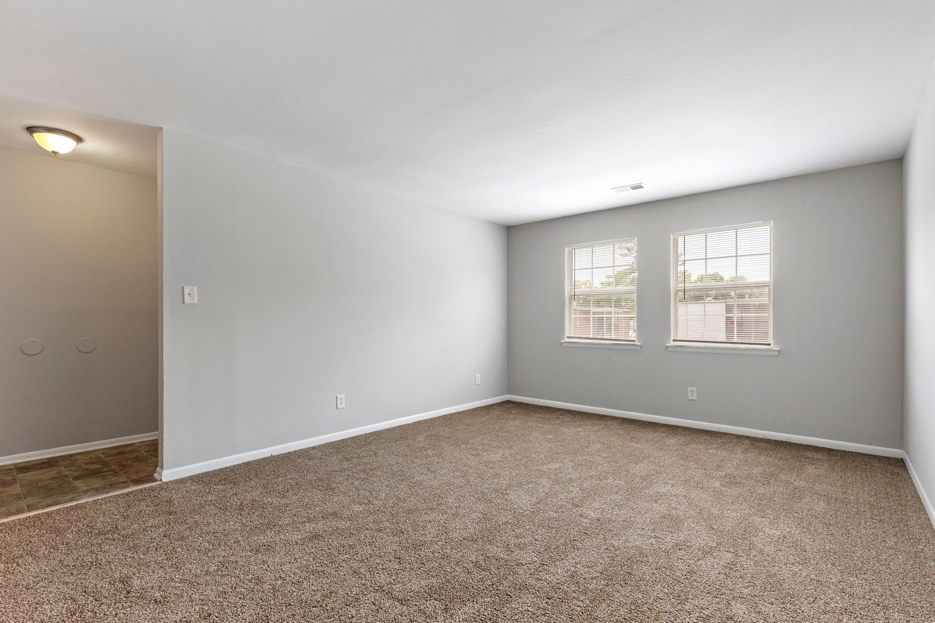 Empty room with gray walls, two windows, and brown carpet. Doorway on left.