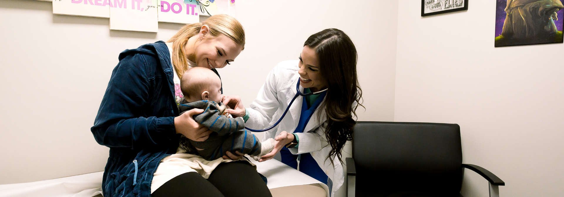 Two people in a clinic examining a baby on a exam table