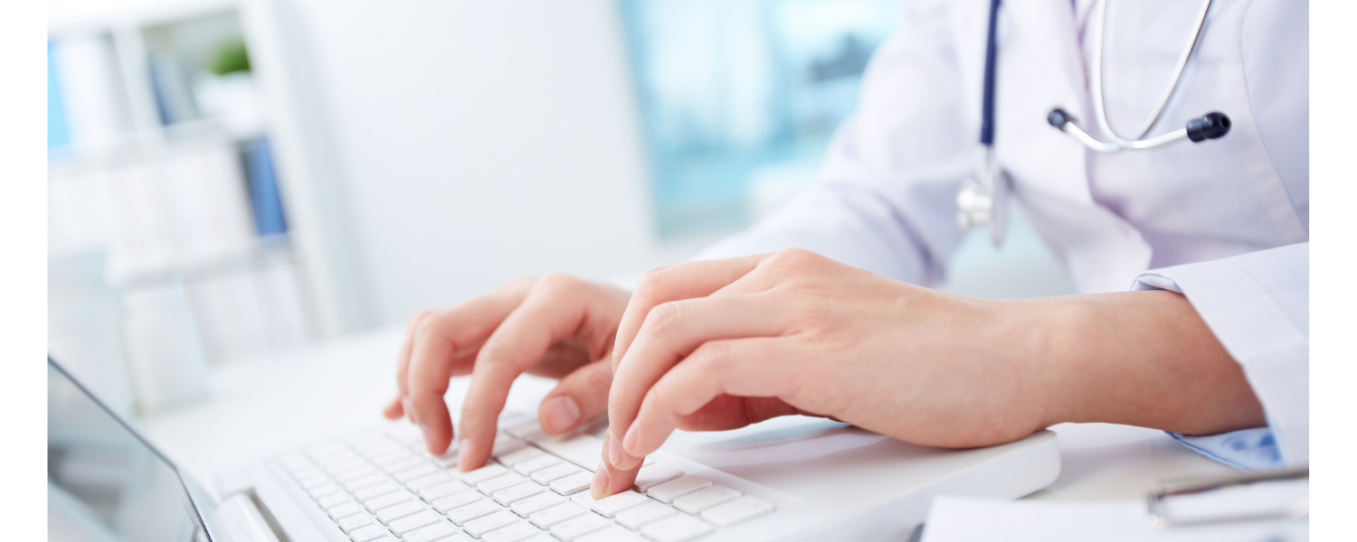 Doctor typing on a keyboard at a bright office desk with a stethoscope around the neck