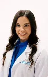 Smiling medical professional in a white coat over blue scrubs against a light background