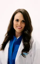 Smiling professional in a white lab coat and blue shirt against a light background