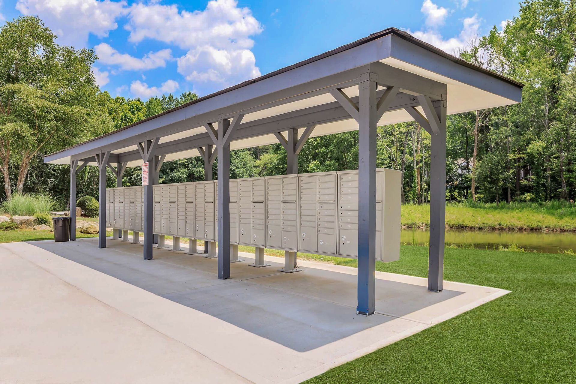Ranch-style house with brick and gray exterior, pillars, surrounded by greenery and lawn.