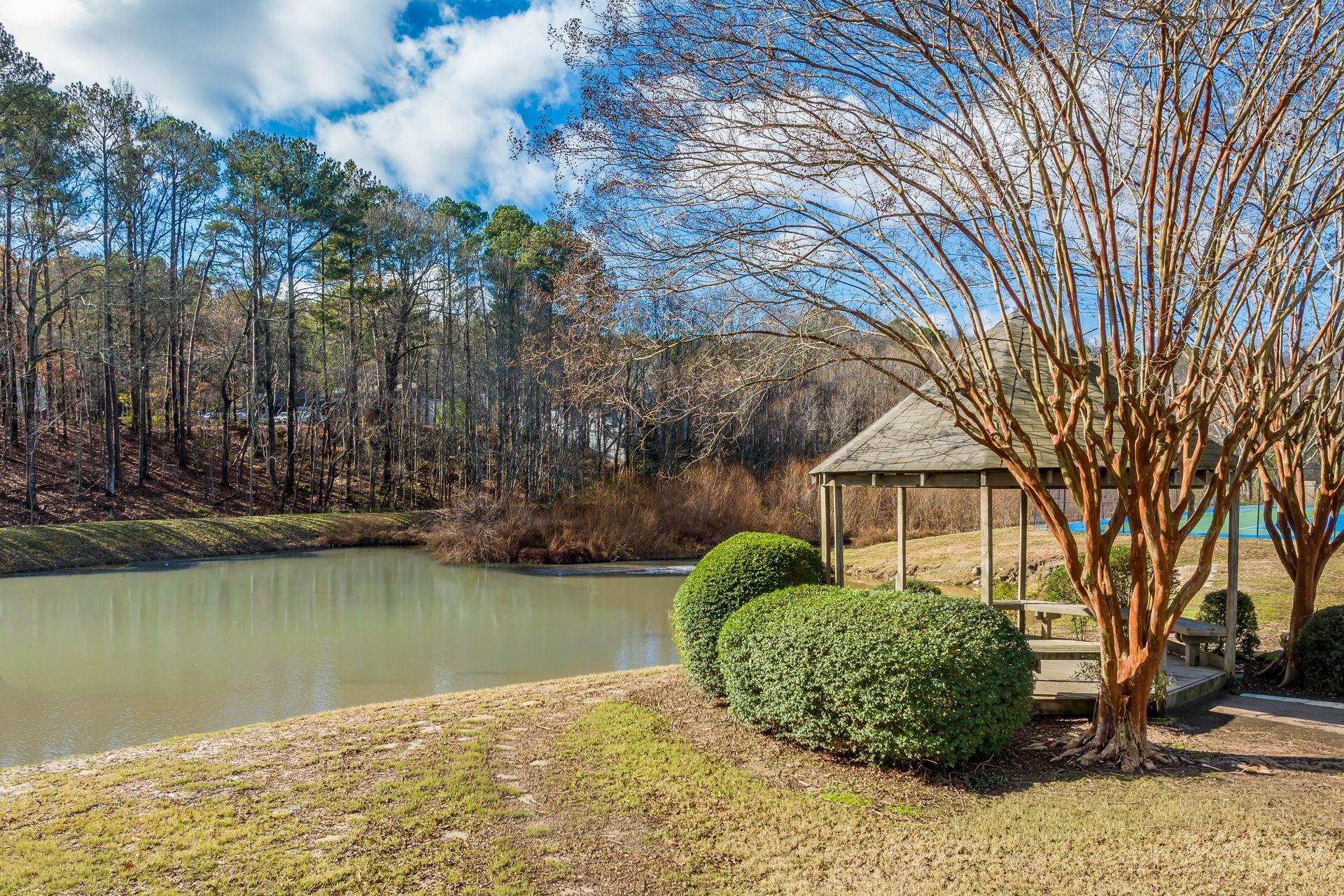 Gazebo in a garden, path leading to it, trees and bushes frame the scene.