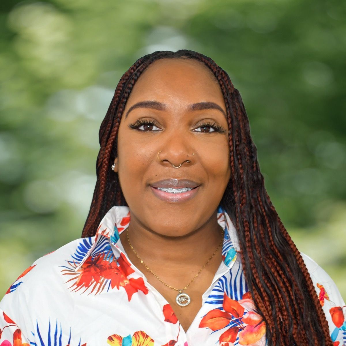 Smiling man with fair skin and a beard in a blue polo shirt, outdoors with green foliage.