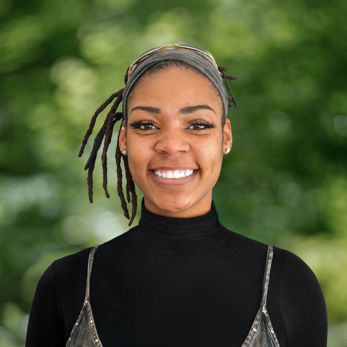 Man with dark hair and beard, wearing striped shirt, smiling, and gazing at the camera, in a bright setting.