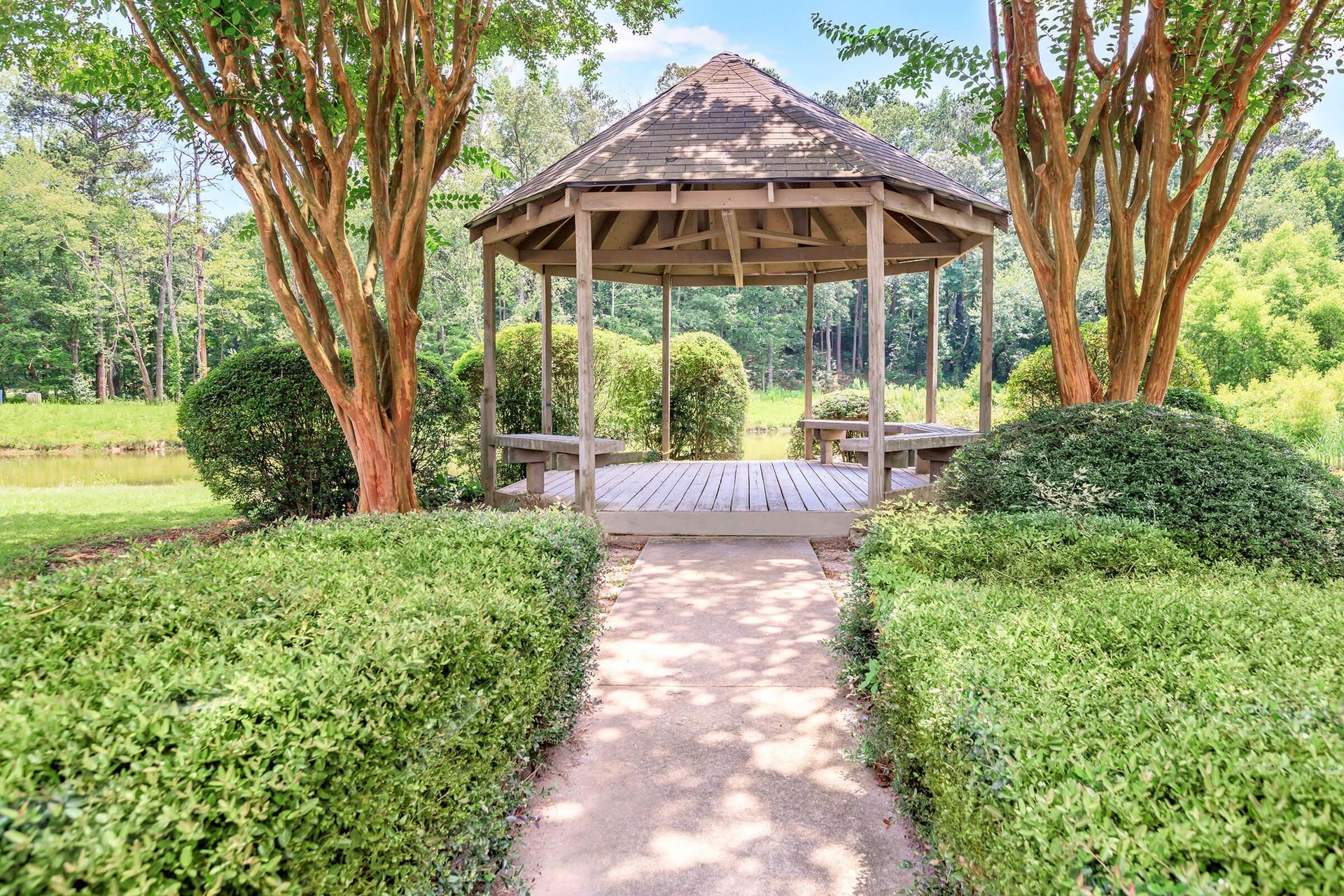 Gazebo in a garden, path leading to it, trees and bushes frame the scene.