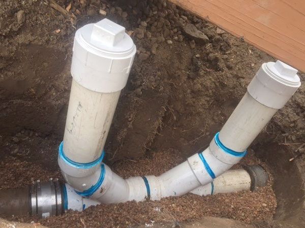 White PVC pipes with capped vertical sections connected to buried horizontal pipe.