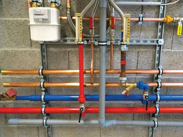Plumbing pipes, including copper, red, and blue, mounted on a concrete wall.