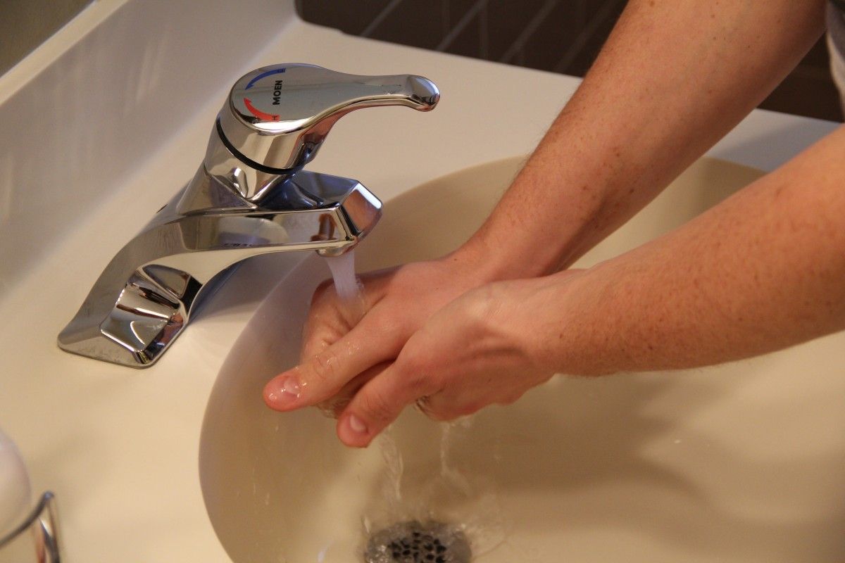 Hands washing under running water in a white bathroom sink.
