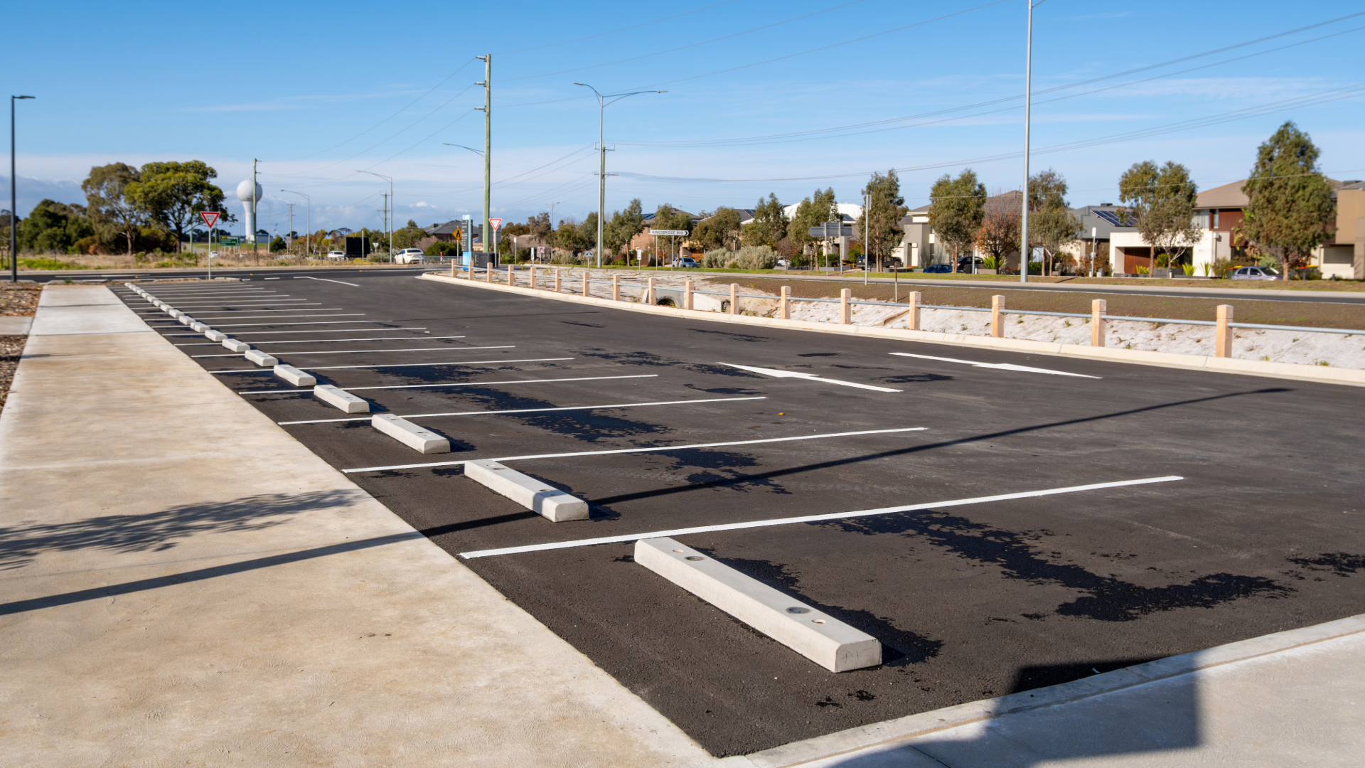 Empty parking lot with fresh black asphalt and white wheel stops under a clear sky