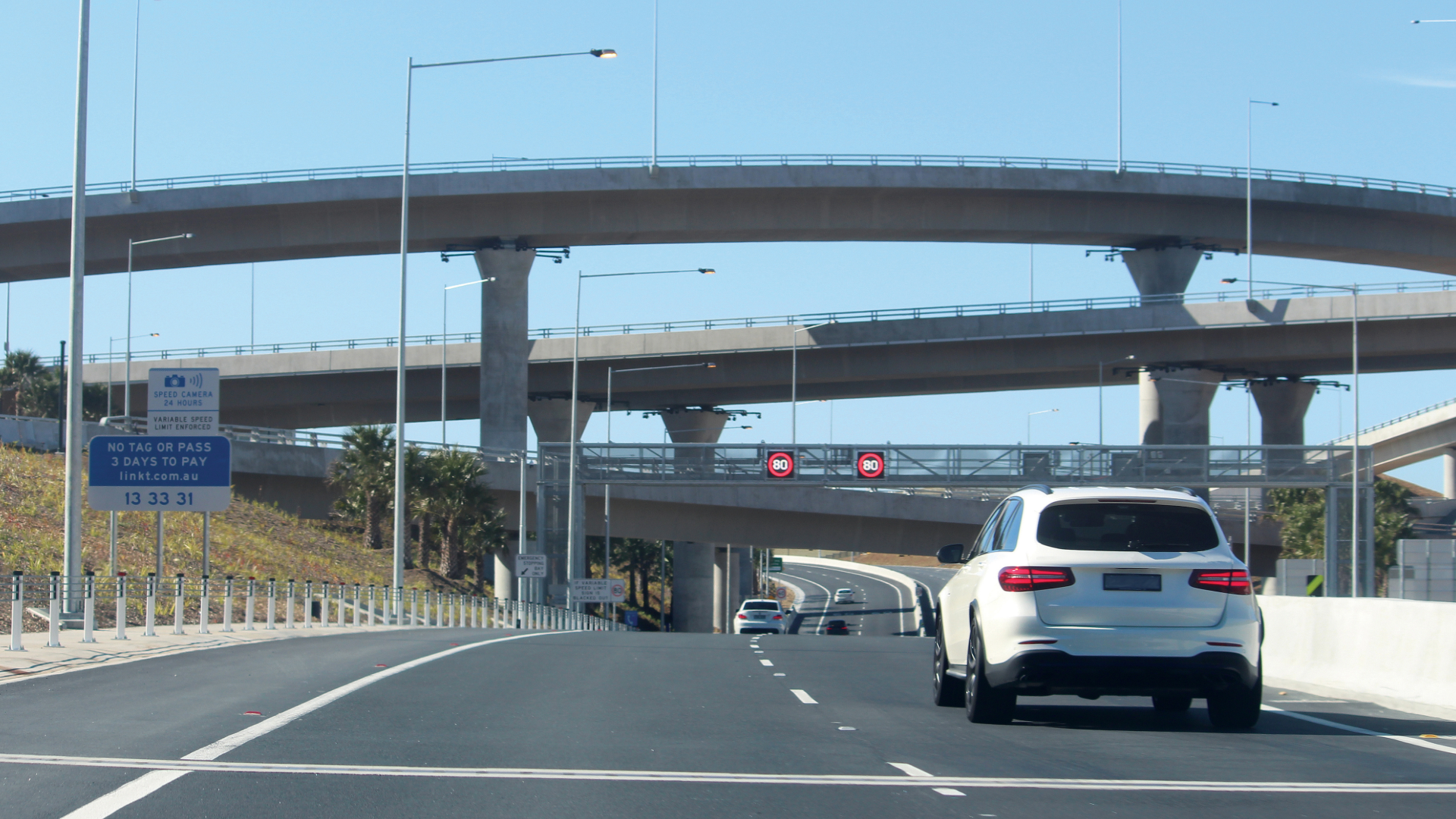 Multi-level highway interchange with a white SUV driving under overpasses on a clear day.