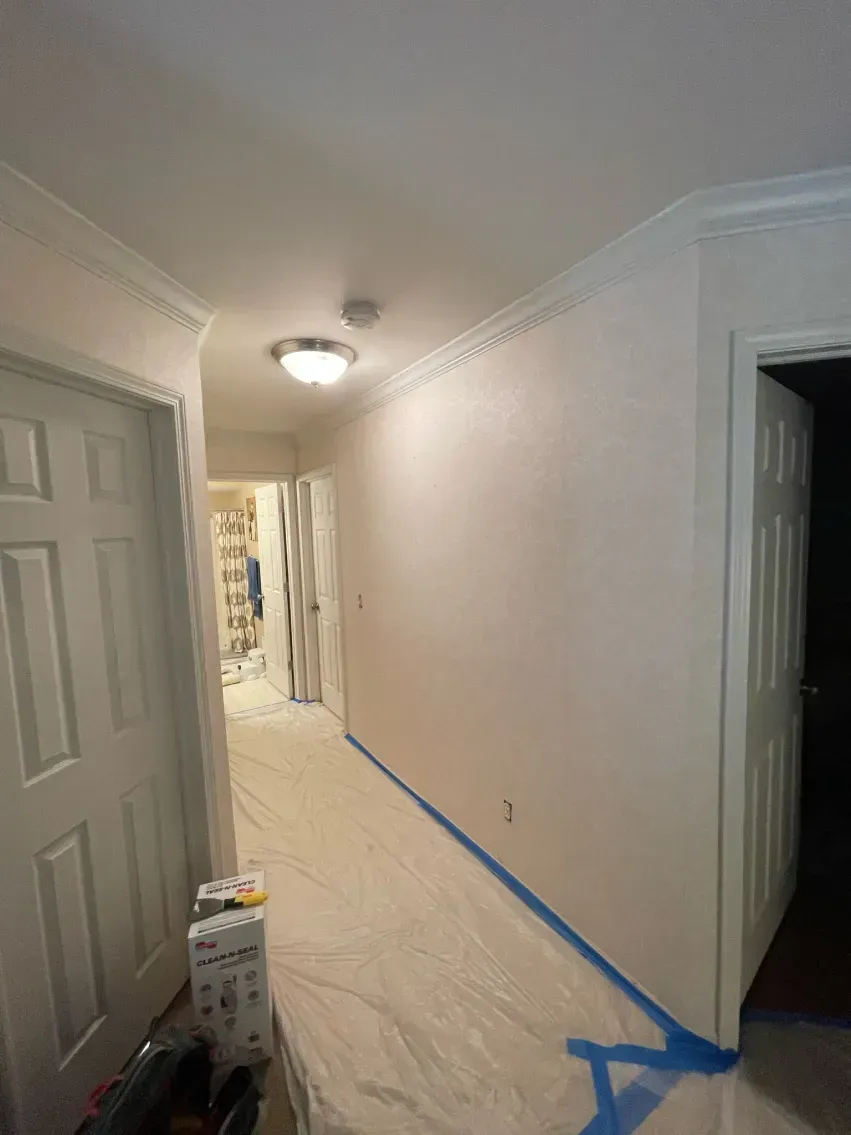 Hallway with white walls, doors, and trim, blue tape on floor, and a light fixture.