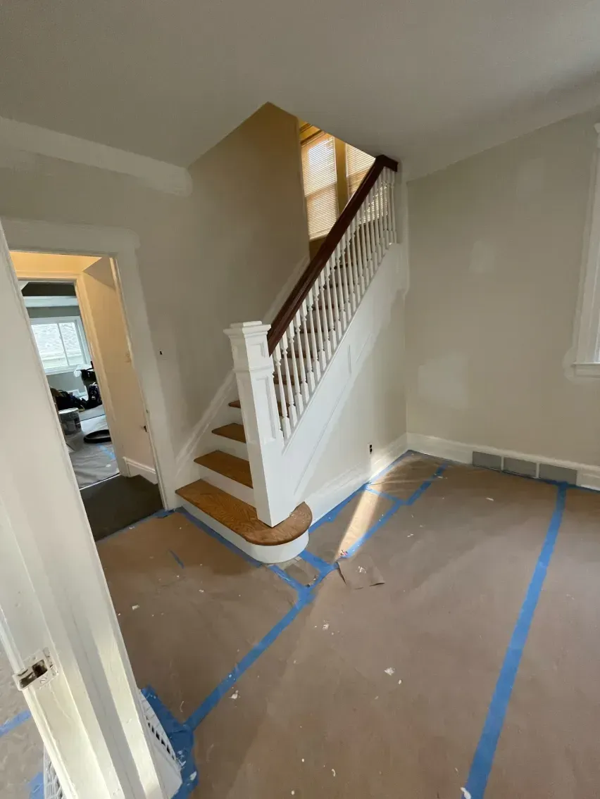Staircase with white railing and wooden steps in a room, taped-off floor, natural light.