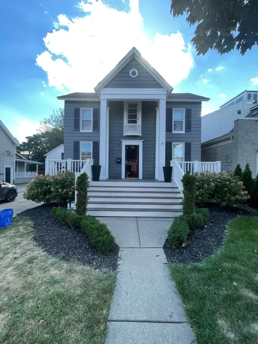 Two-story gray house with white columns and steps leading to the front door. Landscaped front yard with dark mulch.
