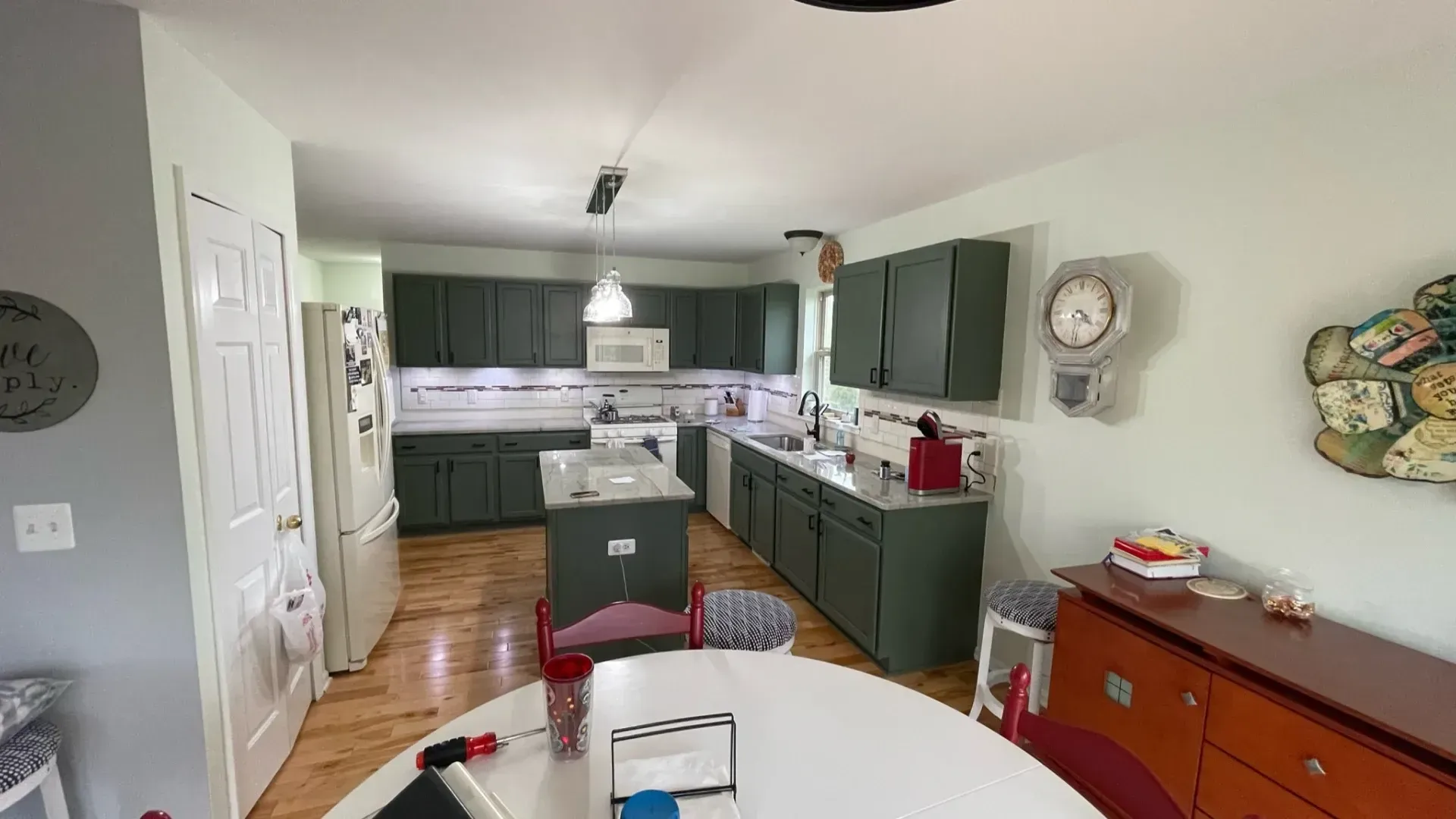 Green-painted kitchen with white appliances, wooden floors, and a round table.